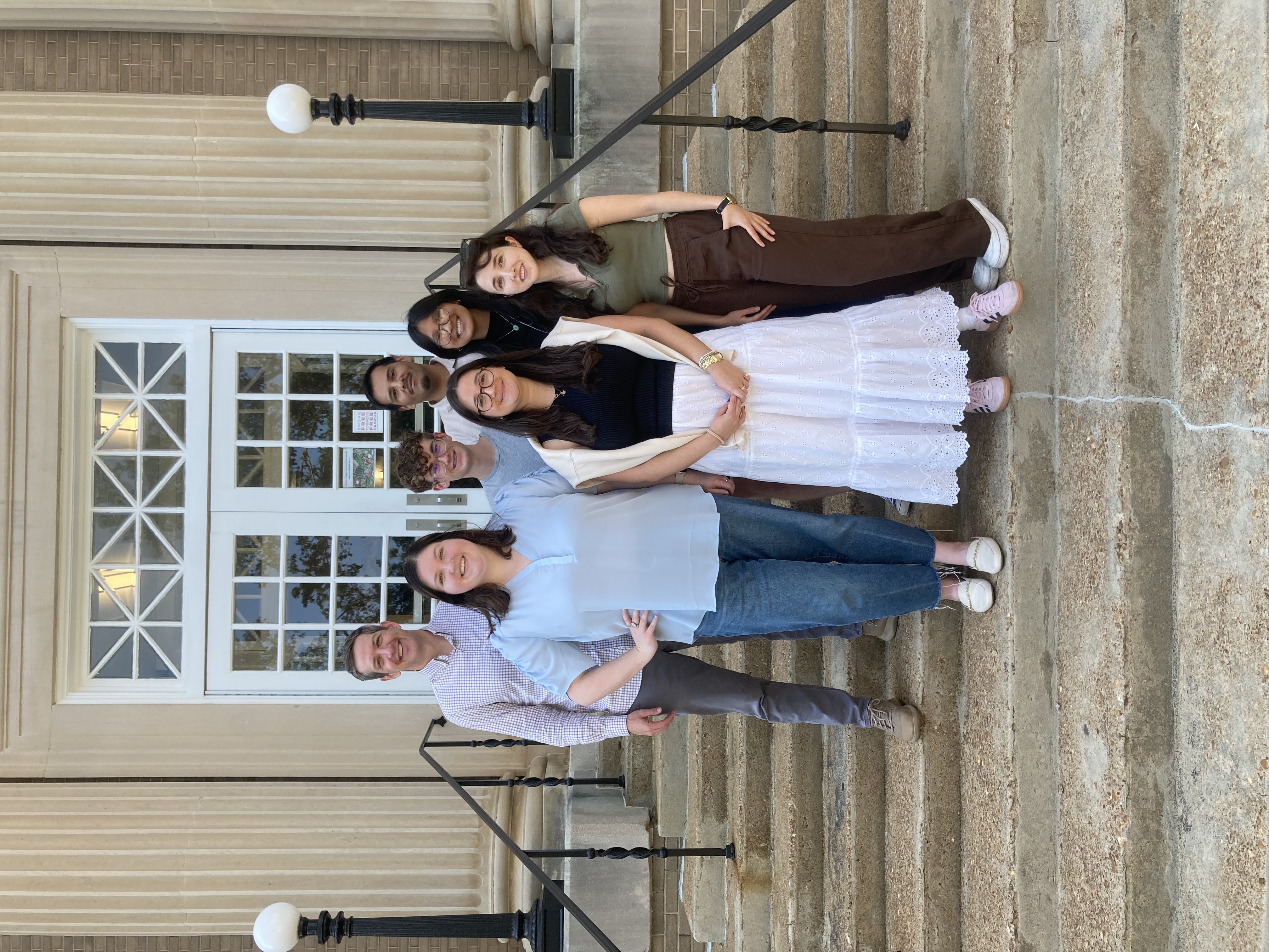 Five people standing on stairs outside a building with windows.