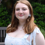 Woman with red hair wearing a white floral dress, smiling.