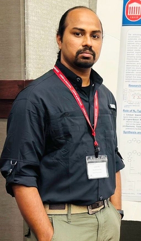 A man wearing a black shirt with a red lanyard stands in front of a poster.