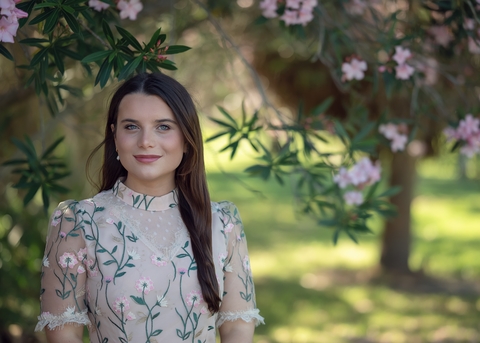 Woman in a pink floral dress standing in front of pink flowers.
