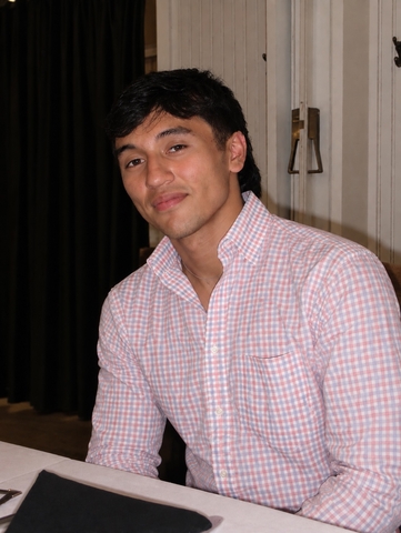 Man in pink and white checkered shirt smiling at camera.