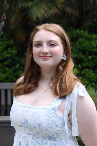 Woman with red hair wearing a white floral dress, smiling.