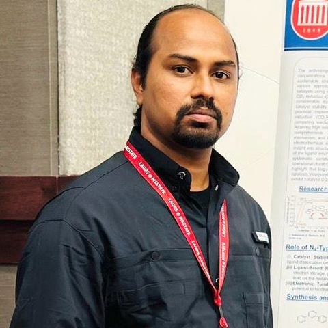 A man wearing a black shirt with a red lanyard stands in front of a poster.