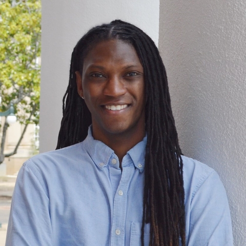 Man with long black hair wearing blue shirt smiling at camera.