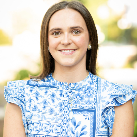 Woman with dark brown hair wearing blue and white printed dress standing outside.