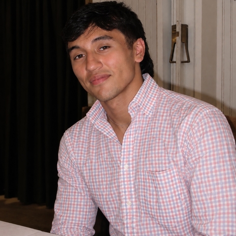 Man in pink and white checkered shirt smiling at camera.