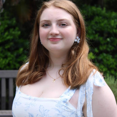 Woman with red hair wearing a white floral dress, smiling.
