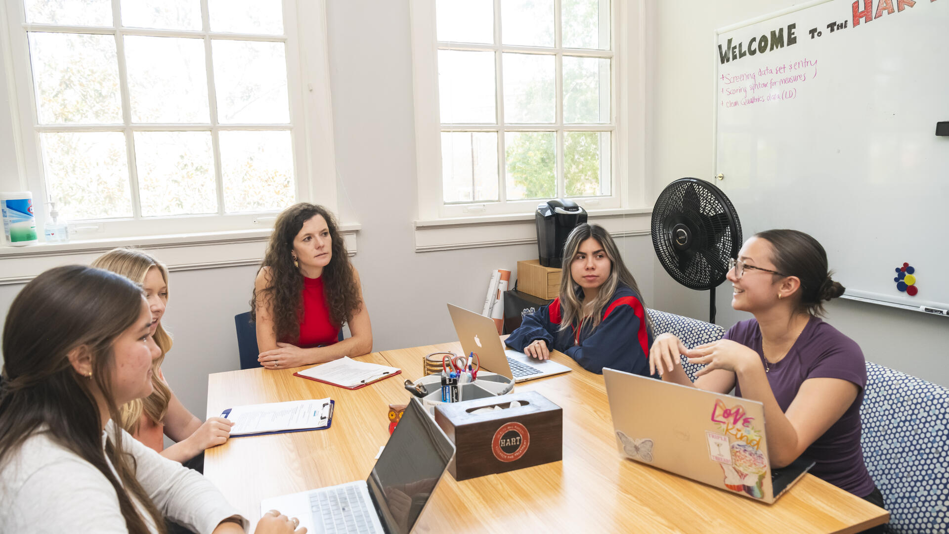group of students and professor sitting around a table with laptops